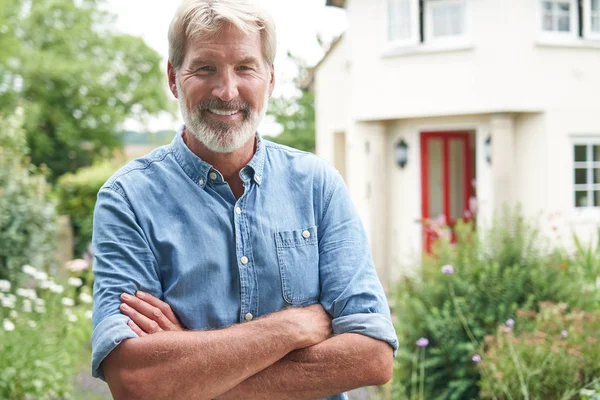 Porträt eines reifen Mannes, der im Garten vor seinem Traumhaus steht — Stockfoto