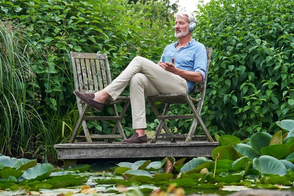Maturo uomo relax in giardino ascolto di musica su wireless hea — Foto Stock