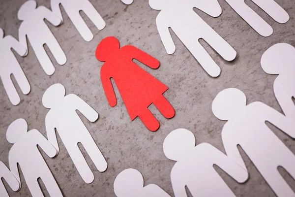 Rood papieren figuur van een vrouw tegen witte silhouetten van mannen. Symbool van seksisme. — Stockfoto