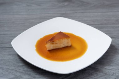 Beyaz bir tabakta açık gri ahşap bir masada duran Napoli kremasının üçgen şeklinde dilimi.