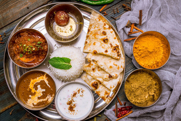 Assorted indian food set on wooden background. Dishes and appetisers of indeed cuisine, rice, lentils, paneer, samosa, spices, masala. Bowls and plates with indian food