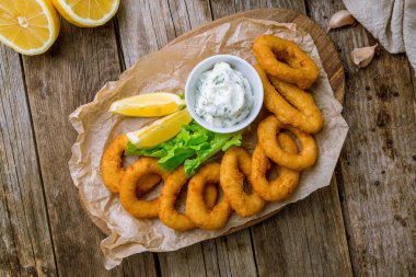 Ahşap arka planda soslu ve limonlu kalamar halkaları.
