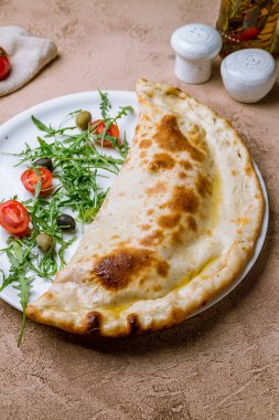 Beyaz tabakta kapalı calzone pizza.