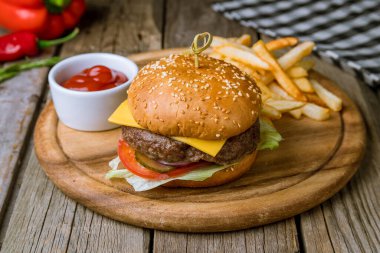 Hamurger, kızarmış patates, peynir ve ketçapla ahşap masada.