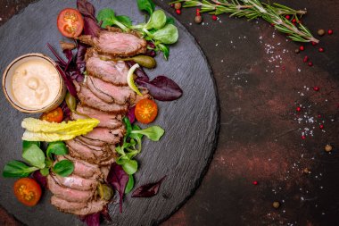 Koyu tabakta salata yapraklarıyla dilimlenmiş biftek. 