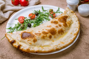 Beyaz tabakta kapalı calzone pizza.