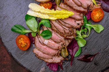 Koyu tabakta salata yapraklarıyla dilimlenmiş biftek. 