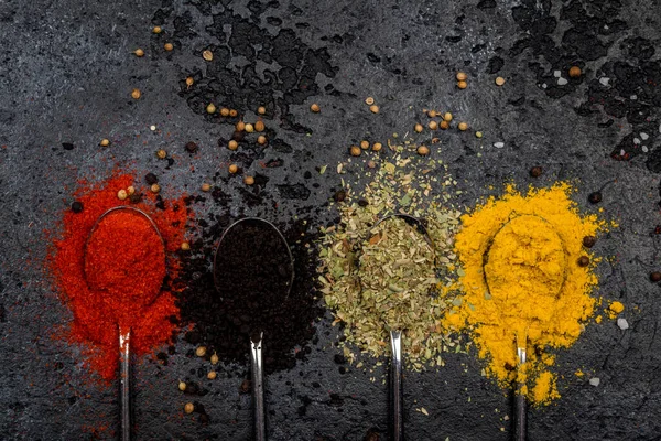 Spices in spoons on dark concrete background
