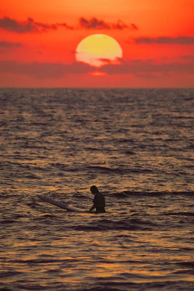 Mulher sentada em uma prancha de surf na frente de um pôr do sol — Fotografia de Stock