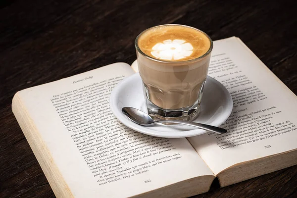 Taza de café capuchino latte caliente o café con leche en una taza de vidrio, libro abierto — Foto de Stock