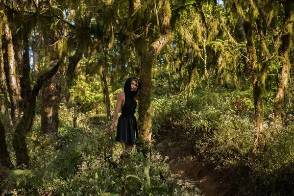 Siyah kapüşonlu bir kız ormanda yürüyor, yürüyüş modasının tadını çıkarıyor.