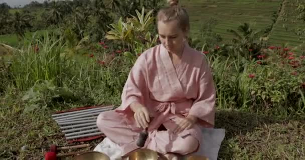 Blondýny žena v růžovém kimonu hraje na meditativní himálajský zpěv mísa. 