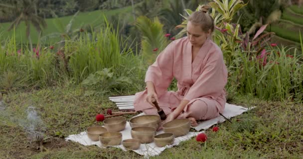 Young woman blonde in a pink kimono plays on a singing bowl — Stock Video