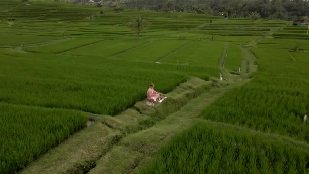 ピンク色の着物を着た女性がバリ島の棚田でボウルを歌っています — ストック動画