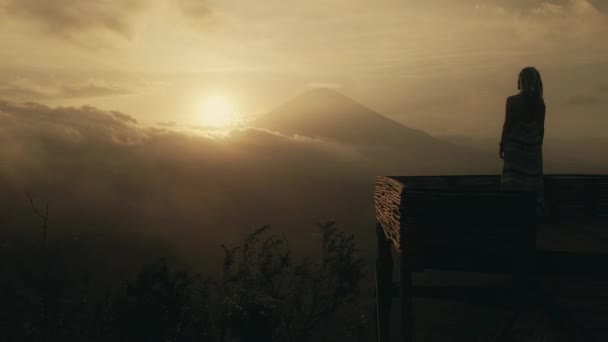 Mädchen in einem langen Kleid steht mit Blick auf den Vulkan Agung auf Bali. Sonnenuntergang — Stockvideo