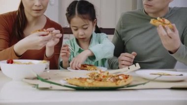 Aile Asyalı insanlar evde lezzetli pizzaların tadını çıkarmaktan mutlu olurlar. Anne-baba ve kızı paket servis servisinden lezzetli İtalyan yemekleri yiyorlar. Yemek siparişini kabul et.