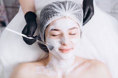 Profesyonel kozmetik uzmanının elleri kaplıca salonunda müşterinin yüzüne maske takar. Kozmetik dolabınızın veya kaplıcanızın reklamını yapmak için ideal bir ortam.