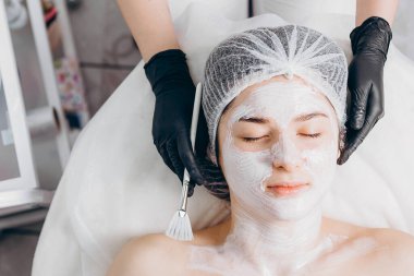 Profesyonel kozmetik uzmanının elleri kaplıca salonunda müşterinin yüzüne maske takar. Kozmetik dolabınızın veya kaplıcanızın reklamını yapmak için ideal bir ortam.