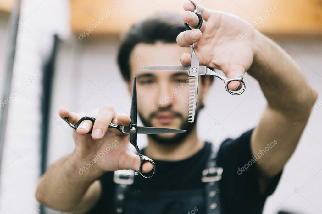 a stylish and attractive bearded barber holds professional hair clippers on his outstretched arms. Focus on the scissors. concept for barbershops, beauty salons and hairdressers