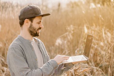 Parkın ortasında dizüstü bilgisayarı olan sıradan giysili genç bir adam.