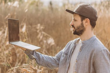 Parkın ortasında dizüstü bilgisayarı olan sıradan giysili genç bir adam.