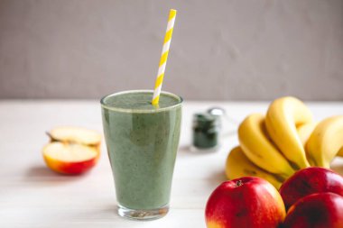 Sağlıklı bir işletme için meyve kokteylinin tanıtım çekimi. Fotoğrafta, meyve ve alg spirulinasından yapılmış yeşil bir içecek bardağı var.