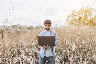 Serbest çalışma konsepti. Yeşil çimlerde oturan ve dizüstü bilgisayar kullanan bir iş adamı. Güneşli bir günde parkta bilgisayarla çalışan sakallı bir adam. Açık havada doğa yolculuğu ve rahatlama.. 