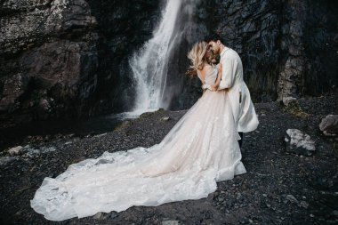 Gürültü efekti, seçici odak: düğün modeli çekimi, şelale arka planında son derece güzel uzun bir elbise ve damat giymiş çekici bir gelin.