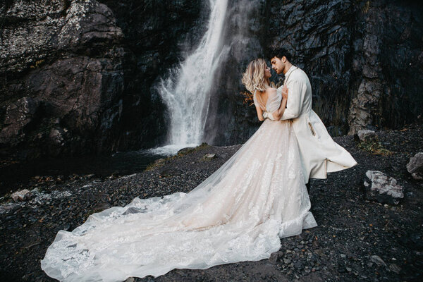 Noise effect, selective focus: wedding couple model shoot, attractive bride in an incredibly beautiful long-flowing dress and groom in a waterfall background