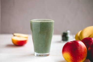 Sağlıklı bir işletme için meyve kokteylinin tanıtım çekimi. Fotoğrafta, meyve ve alg spirulinasından yapılmış yeşil bir içecek bardağı var.