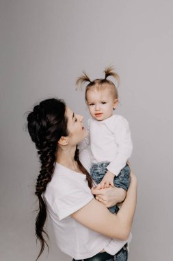 Açık renk elbiseli bir kadın, küçük tatlı bir kızla eğleniyor. Anne, küçük kız beyaz duvar arkasında izole edilmiş, stüdyo portresi. Anneler Günü aşk ailesi, çocukluk kavramı