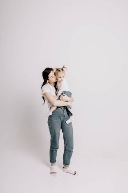 Açık renk elbiseli bir kadın, küçük tatlı bir kızla eğleniyor. Anne, küçük kız beyaz duvar arkasında izole edilmiş, stüdyo portresi. Anneler Günü aşk ailesi, çocukluk kavramı