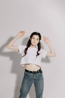 Beyaz tişört ve kot pantolon giymiş atölye ışığı önünde beyaz arka planda fotoğraf için poz veren at kuyruklu güzel bir kadın.