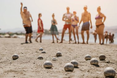 Tatilcilerle dolu bir otelin yanındaki plajda Petanque oynayan arkadaş canlısı insanların portresi.
