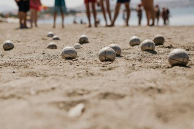 Tatilcilerle dolu bir otelin yanındaki plajda Petanque oynayan arkadaş canlısı insanların portresi.