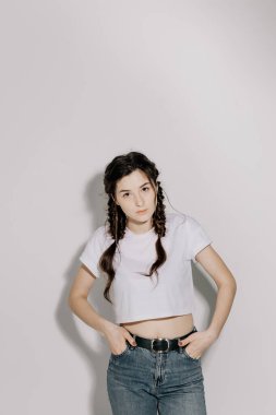 Beyaz tişört ve kot pantolon giymiş atölye ışığı önünde beyaz arka planda fotoğraf için poz veren at kuyruklu güzel bir kadın.