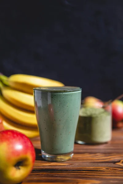 The concept of food and drink, diet and nutrition. Healthy green vegan smoothie with banana, spirulina and ripe apple for summer detoxification