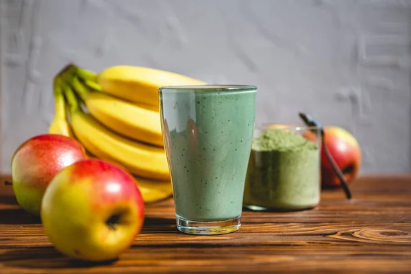 The concept of food and drink, diet and nutrition. Healthy green vegan smoothie with banana, spirulina and ripe apple for summer detoxification