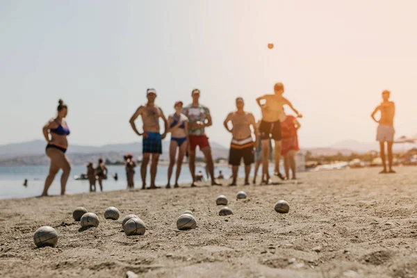 Tatilcilerle dolu bir otelin yanındaki plajda Petanque oynayan arkadaş canlısı insanların portresi.