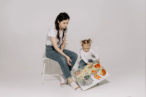 2017ヴィニツァ ウクライナ お母さんは白い背景にスタジオで彼女の赤ちゃんと大きな本を読んでいます — ストック写真