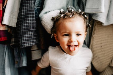 Askıda asılı kıyafetlerin arkasına saklanan bir çocuğun portresi. Karantina oyunları, ebeveynler çocuklarıyla saklambaç oynuyor. Ev yapımı saklambaç oyunu.