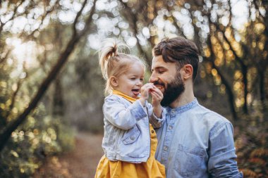 Genç, şık sakallı bir baba gün batımında küçük kızıyla birlikte doğada yürüyor. Baba ve çocuğun aile fotoğrafları. seçici odak, gürültü etkisi