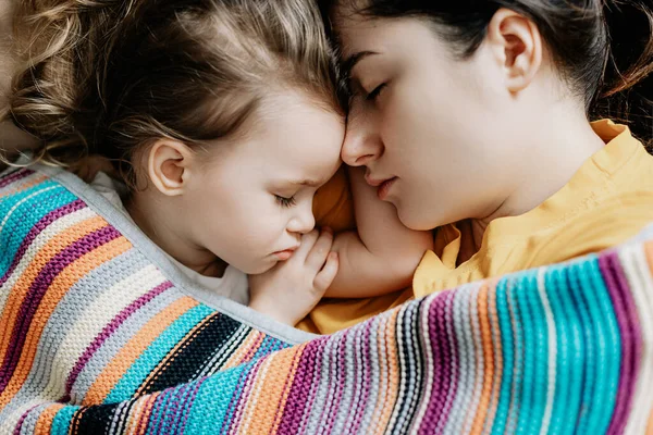 Young mother and baby of 2 years sleep together hugging, daytime sleep concept for children. Mom fell asleep with her baby while putting her to sleep