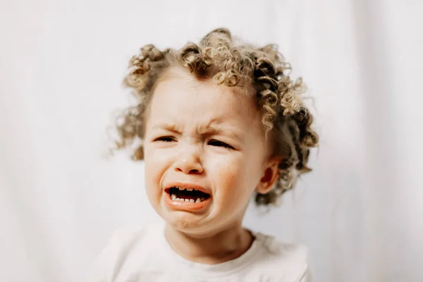 Little curly girl is crying very emotionally, face with tears and negative emotions of disappointment and insult. Baby emotions and baby crying