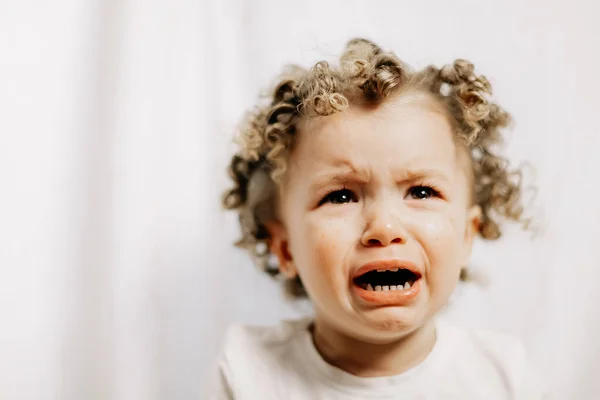 Little curly girl is crying very emotionally, face with tears and negative emotions of disappointment and insult. Baby emotions and baby crying