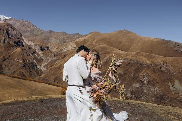 Bride in love on the top of the mountain: wedding photo shoot under a stylish arch, attractive man in a national Georgian costume and bride in a sophisticated dress