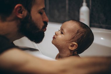 seçici odaklanma, gürültü etkisi: sakallı baba bebeği banyoda yıkıyor ve yıkıyor, çocuk kız eğleniyor, o mutlu ve gülümsüyor, suyun tadını çıkarmayı seviyor
