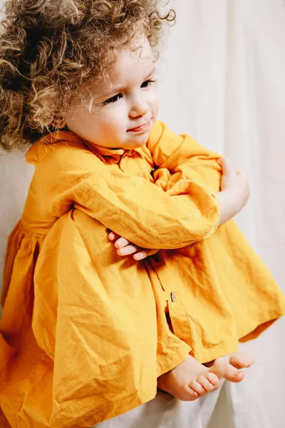 Portrait of a little curly girl with freckles dressed in a yellow dress Home family fun parents with baby.