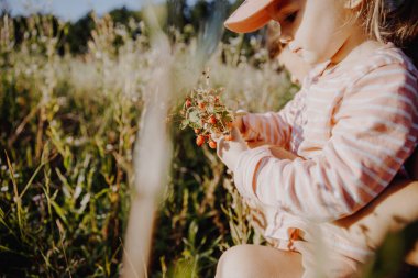 Pembe elbiseli küçük kız bahçede bitkilerle oynuyor.