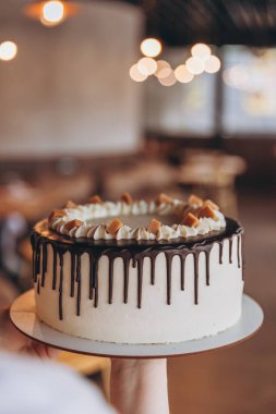 Kafe arka planında çikolata ve karamel olan iştah açıcı büyük beyaz pasta.